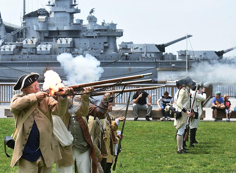 Fall River firepower is well in evidence, as a Minuteman touches off his Brown Bess musket at advancing British troops, with the guns of Big Mamie remaining silent in the background, during a re-enacted skirmish -- part of the 240th anniversary of the Battle of Fall River, on Saturday, June 2, 2018, at Heritage State Park in Fall River, Massachusetts. [Herald News Photo | Jack Foley]