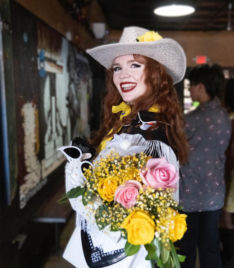 CJ Scott, winner of the Route 66 Pinup Pageant, poses with a bouquet and a smile inside the 806 Coffee Shop in Amarillo, capturing the pageant’s retro charm and Western flair.