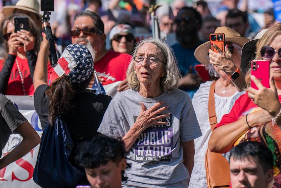 A woman places her hand over her heart while wearing a "Public Radio" t-shirt during the national anthem at the "No Kings" demonstration on June 14, 2025 in San Antonio, Texas. The protest was part of nationwide demonstrations against Trump administration immigration policies.