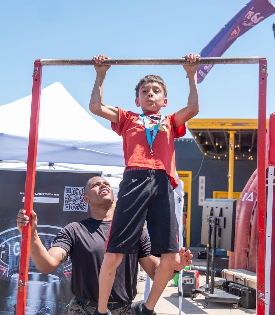 A young boy completes a pull-up with help from a U.S. Marine during a strength challenge at the Route 66 Festival, one of several family-friendly activities offered.